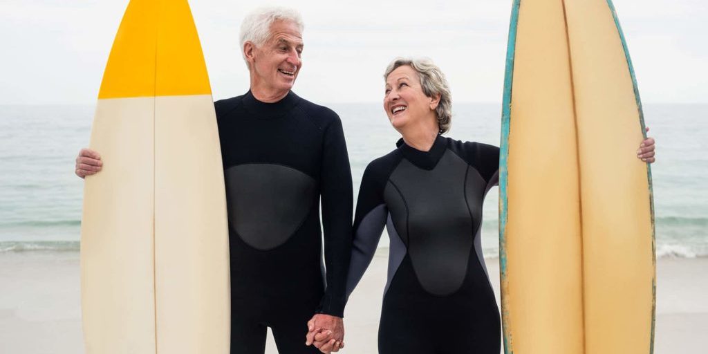 Older couple holding hands standing with two surf boards.